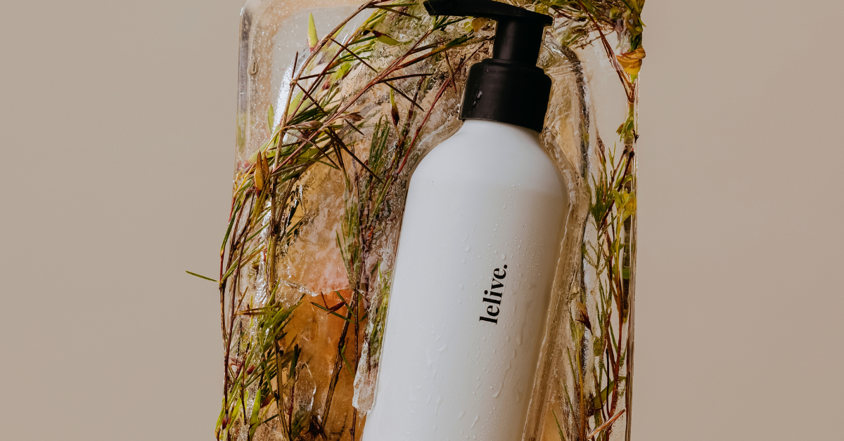 lelive pump bottle set in a block of ice with botanical grasses and stems frozen throughout, against a warm neutral background